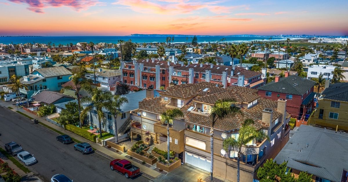 Aerial view of a coastal San Diego neighborhood at sunset with homes lining the street and the ocean beyond
