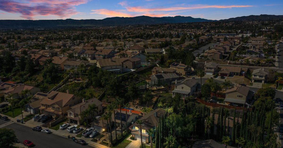 Aerial view at sunset of an established San Diego County residential neighborhood with tile-roof homes and mountains on the horizon